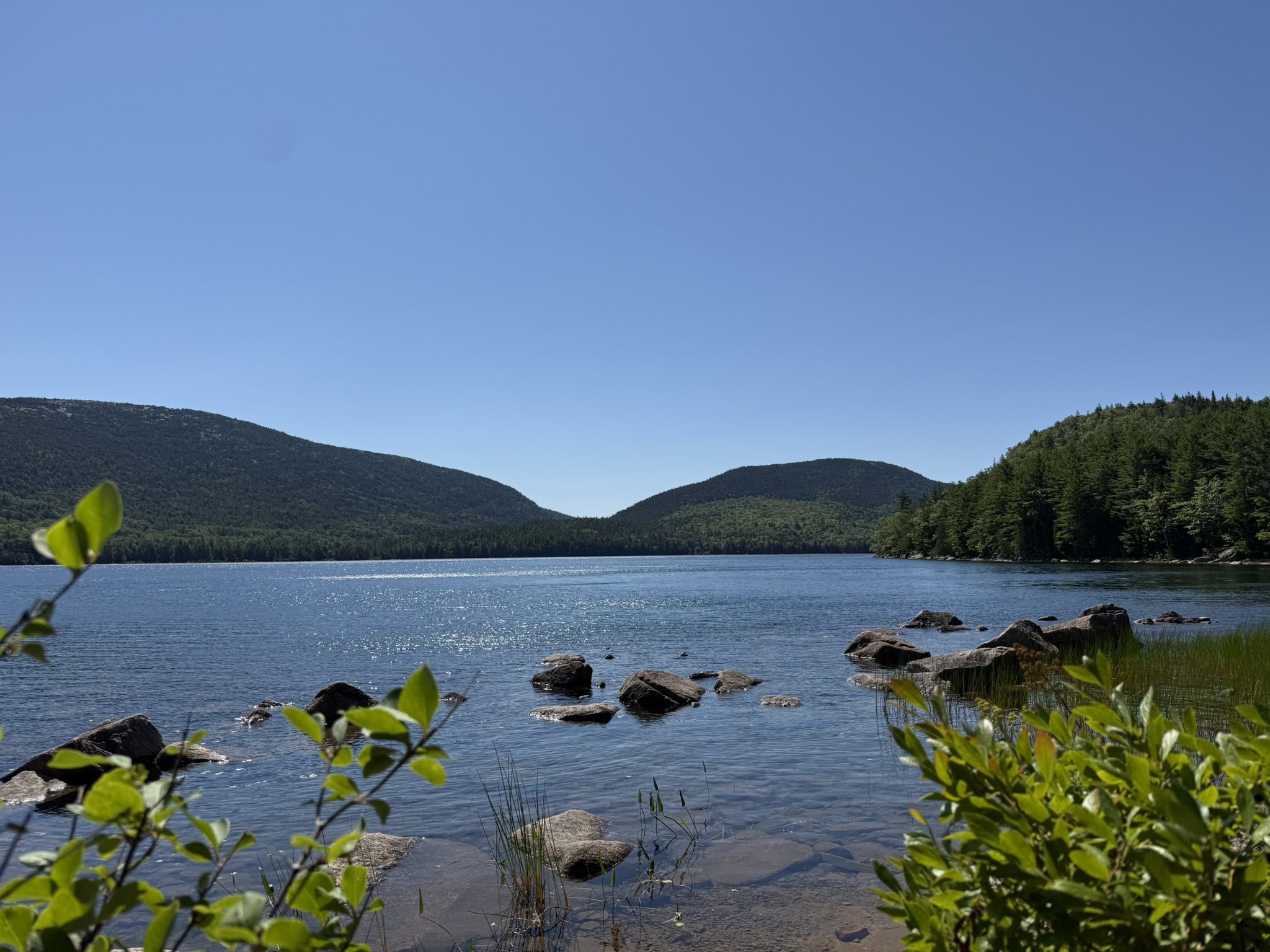 A peaceful lake with rocks, mountains, and a clear blue sky.